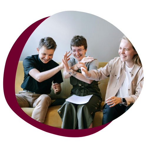 Three teenagers sit on a couch and high-five one another. 